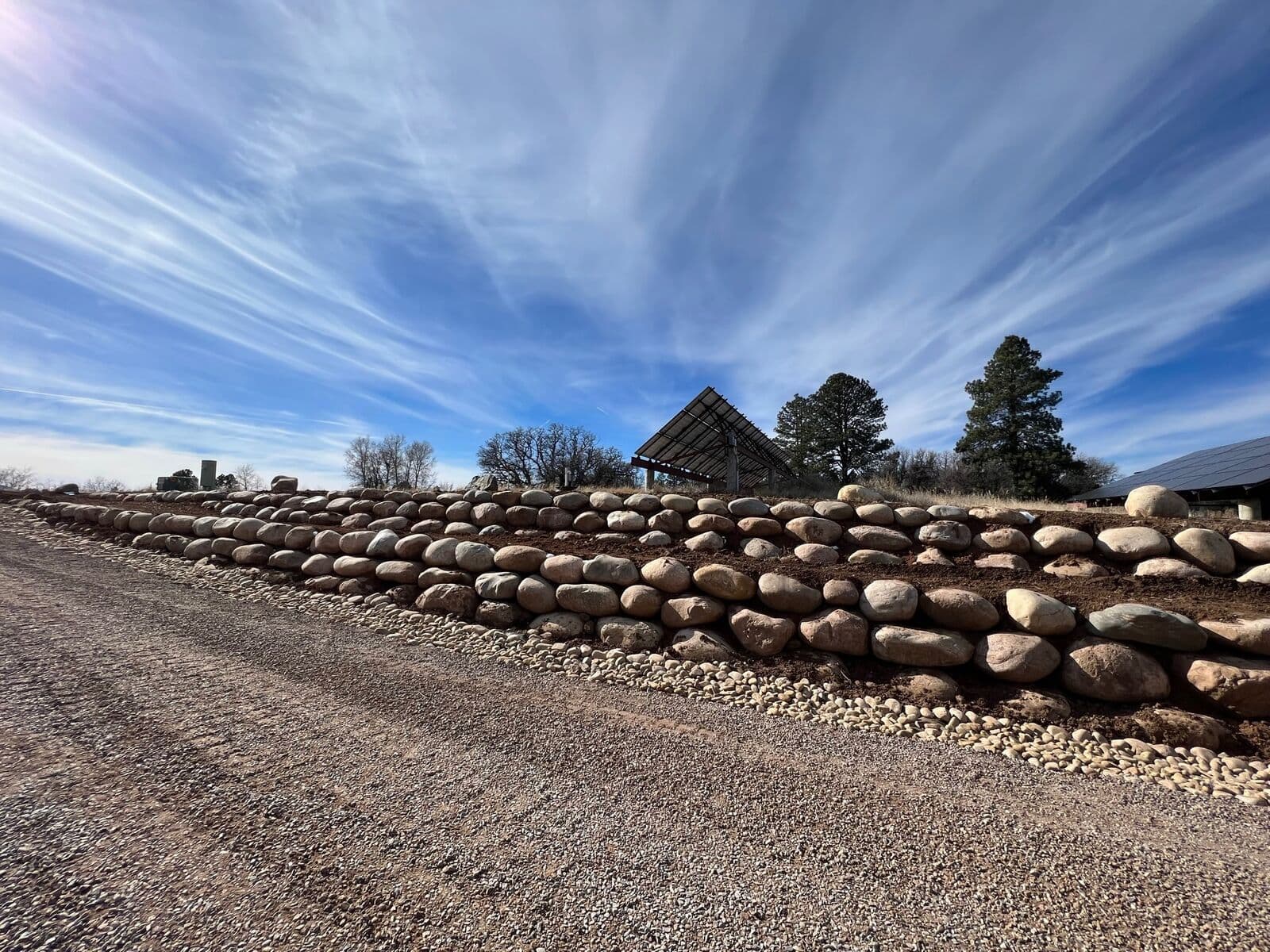 Boulder retaining wall along a gravel road under dramatic Colorado skies