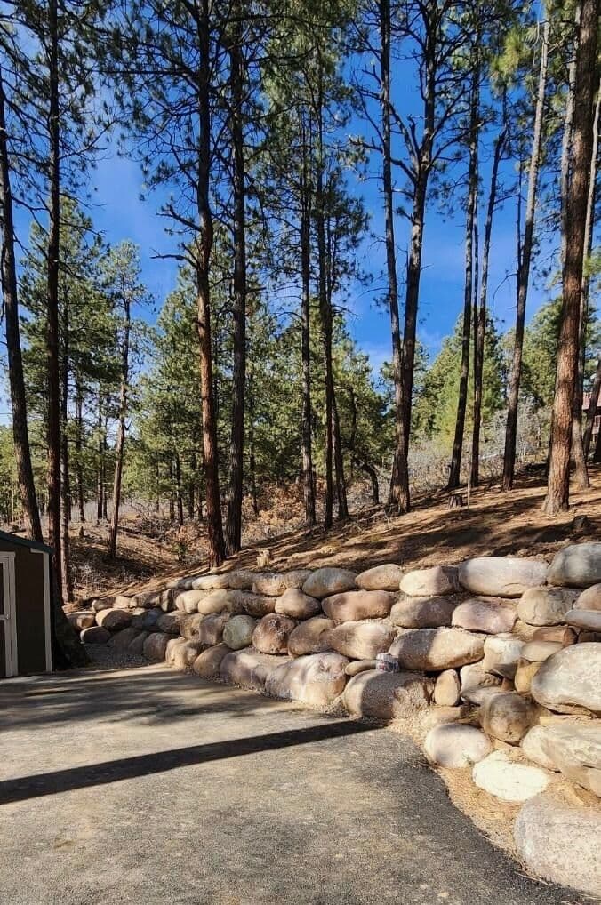 Boulder retaining wall along an asphalt driveway under pines in Durango, Colorado