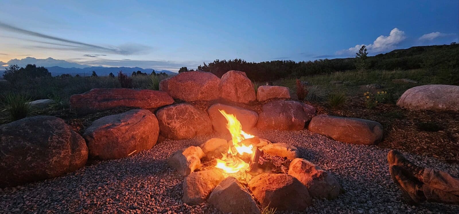Custom boulder fire pit glowing at dusk on a Durango, Colorado property by LandEx Earthworks