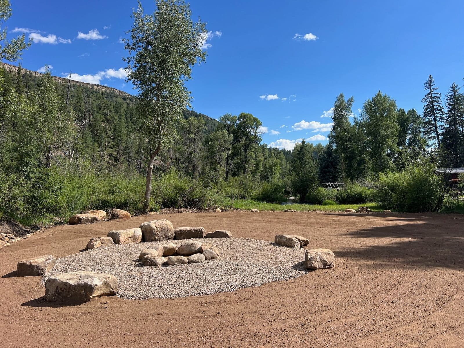 Gravel fire pit area with natural boulder seating beside the river near Durango, Colorado by LandEx Earthworks