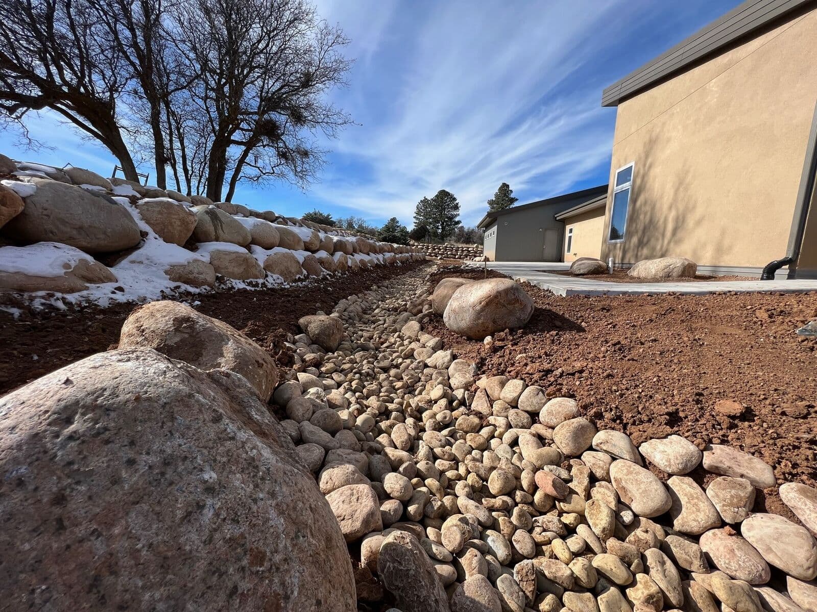 River rock drainage swale with boulder placement at a stucco home near Durango, Colorado by LandEx Earthworks