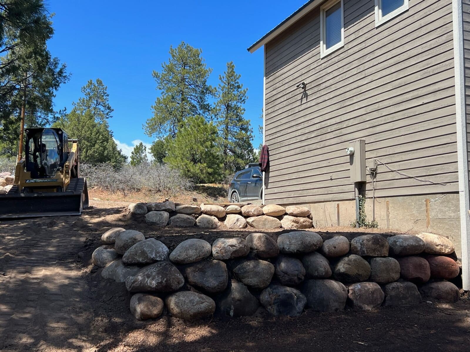 Skid steer building a boulder retaining wall behind a home in Durango, Colorado