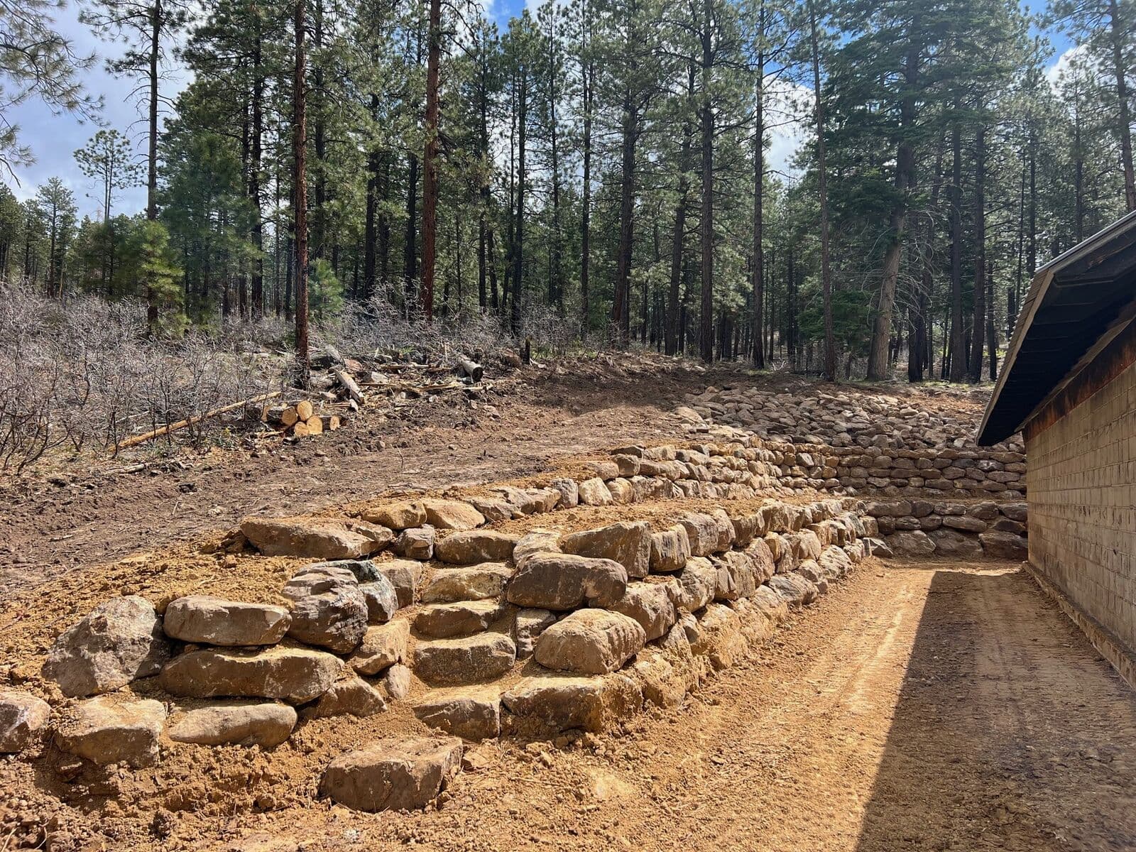 Terraced boulder retaining wall with natural stone steps on a forested hillside in Durango, Colorado by LandEx Earthworks