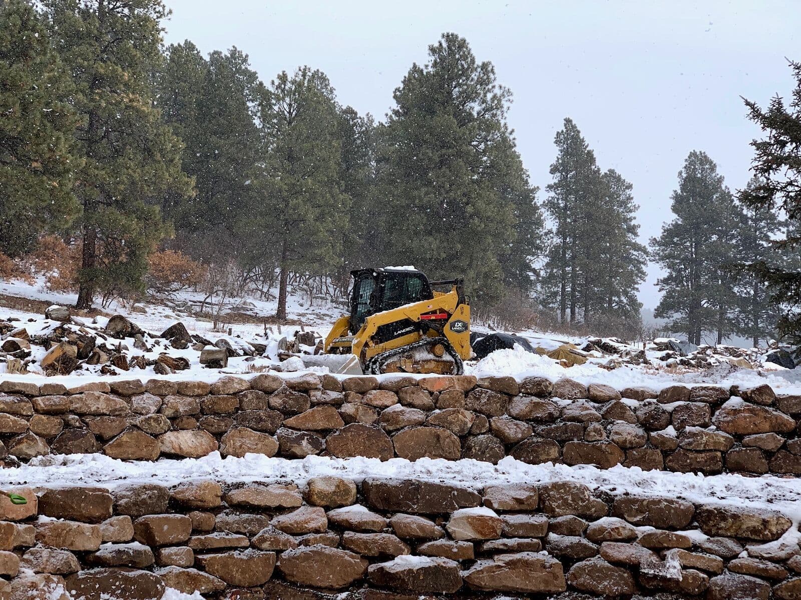 Skid steer placing boulders for a terraced retaining wall in winter near Durango, Colorado by LandEx Earthworks